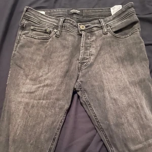 Grå jeansbyxor med normal passform - Säljer ett par grå jeansbyxor med klassisk femficksdesign och knappgylf. Byxorna har en något tvättad look och raka ben. Perfekta till vardags och passar till det mesta. Märke Jack and Jones