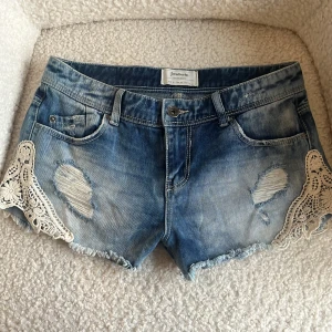Blå jeansshorts med spets från Stradivarius - Blå lågmidjade jeansshorts med spets. Supersnygga men säljer då de tyvärr inte passade.💗