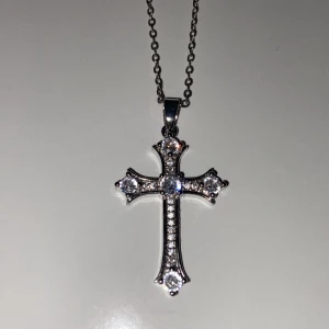 Silverfärgat korshalsband med stenar - Snyggt halsband med ett korsformat hänge i silverfärg, dekorerat med gnistrande stenar längs hela korset. Kedjan är tunn och stilren, perfekt för att ge en extra touch till din outfit. ‼️OBS, ”Kristallerna” är ej äkta och finns endast för dekoration och touch så att du vet vid köp ‼️