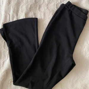 Svarta utsvängda byxor från SHEIN - Svarta byxor från SHEIN med utsvängda ben och hög midja. Byxorna har en enkel design utan synliga detaljer och är tillverkade i ett mjukt, stretchigt syntetmaterial. Perfekta för en stilren och bekväm look.