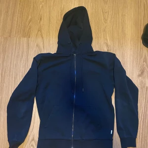 Svart hoodie med dragkedja från Jack & Jones - Säljer en svart hoodie från Jack & Jones i storlek XS. Tröjan har dragkedja framtill, huva med snörning och två fickor. Perfekt för en avslappnad stil och enkel att matcha med det mesta.