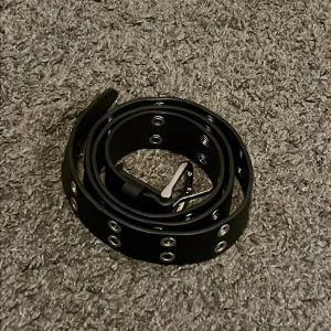 Svart bälte med silverfärgade nitar - Säljer ett svart bälte med flera silverfärgade metallhål längs hela bandet. Bältet har en enkel design och passar till många olika stilar. Perfekt accessoar för att ge outfiten lite edge 🤘🖤