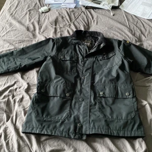 Barbour field jacket - Säljer en svart jacka från Barbour International. Den är regn tålig. Dragkedjan är sönder man går fint att knäppa med knapparna, ingen skillnad. Pris kan sänkas vid snabb affär