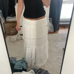 Vit långkjol med spetsdetaljer - Säljer en vit långkjol med bred midja och fina spetsinslag runt om.  Köpt på en marknad för 300kr, ANVÄDN FÅTAL GÅNGER OCH INGA TÄCKEN PÅ ANVÄNDING!💕💕den går nästan ner till marken på mig som är ca 163💕