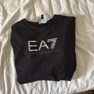 Svart långärmad tröja från Emporio Armani EA7 - Svart långärmad tröja från Emporio Armani EA7 med stor silver logga på bröstet. Klassisk rund halsringning och mjukt material. Riktigt skön bra passform, storlek 160 cm, utmärkt skick. Pris kan diskuteras vid snabb affär