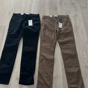 Bruna chinos från NN07 - Snygga bruna chinos från NN07 i klassisk rak passform. Byxorna har knäppning fram och bälteshällor, perfekta för en stilren look. Tillverkade i mjukt bomullsmaterial som ger en bekväm känsla hela dagen. Båda e helt nya med prislapp kvar. Ny pris 1199kr säljer för 400kr styck eller 600kr för båda.