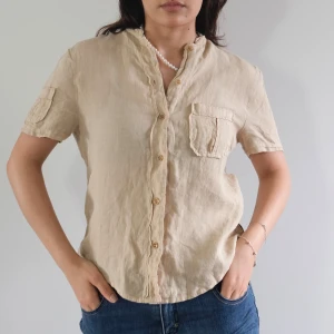 Vintage Armani jeans beige skjorta/topp - Vintage Armani jeans beige skjorta/topp  Beige skjorta med korta ärmar, en bröstficka och knappar framtill. Skjortan har en avslappnad passform. Storlek S  Length:61cm Chest:46cm Shoulder:39cm Arm:15cm