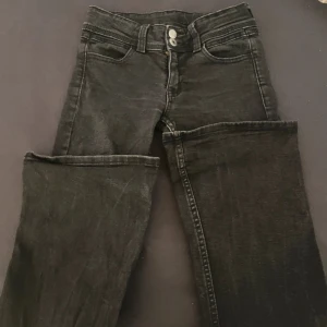 Svarta jeansbyxor med raka ben - Säljer ett par svarta jeansbyxor med raka ben och dubbla knappar i midjan. Byxorna har klassiska fem fickor och dekorativa sömmar på bakfickorna. Perfekta för dig som gillar en enkel och stilren look.