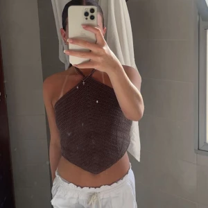 Brun virkad halterneck-topp - Säljer en brun virkad halterneck-topp med asymmetrisk skärning. Toppen knyts i nacken och har en croppad passform som passar perfekt till sommaren. Superfin till både shorts och kjol!