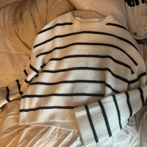 Vit och svart randig stickad tröja från Kappahl - Säljer en vit stickad tröja från Kappahl med svarta horisontella ränder. Tröjan har en rak passform och långa ärmar. Perfekt för dig som gillar en klassisk och enkel stil.