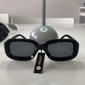 Svarta solglasögon från Prestige - Stilrena svarta solglasögon från Prestige med rektangulära bågar och mörka glas. Klassisk design som passar till många tillfällen. Snygg accessoar för dig som vill ha en tidlös look.