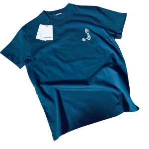 Mörkblå Jacquemus t-shirt 🎣 - Mörkblå Jacquemus t-shirt 🎣 Vit broderad fisk på bröstet & stor logga på ryggen. Storlek S men sitter som M/L – inte för dig som vanligtvis har S. Helt ny med tags, aldrig använd ✅ Nypris: 2500 kr. Pris kan diskuteras vid snabb affär 💬 Stilren med en twist – hör av dig vid intresse!