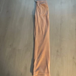Ljusrosa mjukisbyxor från Juicy Couture - Säljer ett par ljusrosa mjukisbyxor från Juicy Couture med bred resår i midjan och snörning. Byxorna har stora fickor fram och bak med knappdetaljer och är i mjuk velour. Perfekta för en avslappnad stil.