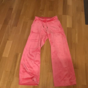 Rosa mjukisbyxor med dragsko - Säljer ett par rosa mjukisbyxor med breda ben och dragsko i midjan. Byxorna har fickor framtill och är gjorda i ett mjukt, syntetiskt material som känns skönt mot huden. Perfekta för en avslappnad stil.