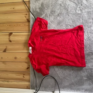 Röd t-shirt från Comme des Garçons Play - Säljer en klassisk röd t-shirt från Comme des Garçons Play med liten broderad logga på bröstet. T-shirten har rund hals och korta ärmar. Perfekt för dig som gillar stilrena plagg med en twist.