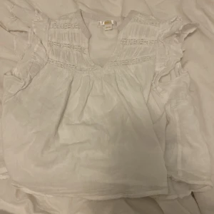Vit blus med volang från Gina Tricot - Säljer en söt vit blus från Gina Tricot med volangdetaljer vid axlarna och v-ringning. Blusen har fina broderade partier upptill och är tillverkad i ett lätt och luftigt material. Perfekt för varma dagar! Pris kan diskuteras❤️