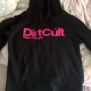 Svart hoodie från DirtCult San Diego - Svart DirtCult hoodie med rosa tryck. Använd fåtal gånger!