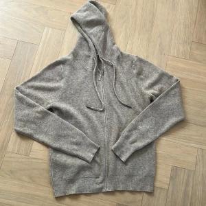 kashmir hoddie - Mysig grå kashmir hoodie med dragkedja framtill och justerbar huva. Perfekt för lager-på-lager och passar till många olika stilar. Långa ärmar och ribbade muddar ger en skön passform. Inte riktig kashmir