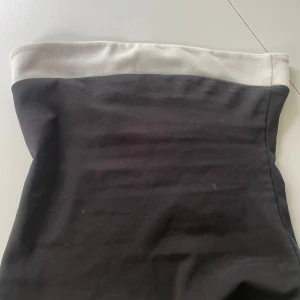 Svart och vit tubtopp från Boohoo - Säljer en svart och vit tubtopp från Boohoo. Toppen är axelbandslös och har en enkel, stilren design med svart kropp och vit kant upptill. Perfekt att styla till jeans eller kjol för en trendig look.