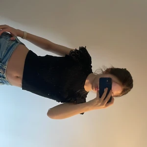 Svart ribbad topp med volangärmar - Säljer en svart ribbad topp med korta volangärmar i broderad spets. Toppen är croppad och har en rund halsringning. Perfekt för dig som vill ha en söt och trendig look. Köpte den 1 år sedan från Zara.