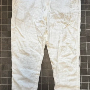Vita linnebyxor från Zara - Snygga vita byxor från Zara i en blandning av linne och bomull. De har normal passform, dragsko i midjan och klassisk knappgylf. Perfekta för en fräsch och avslappnad stil under varma dagar.