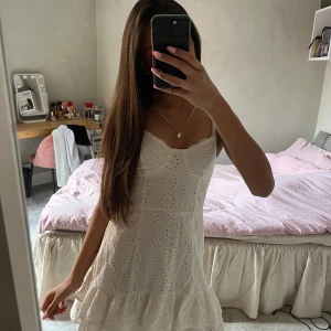 Vit volang klänning - Superfin vit klänning med blommor och volanger från bershka. Axelbandslös modell med smock i ryggen för skön passform. Perfekt för varma dagar och midsommarfirande.