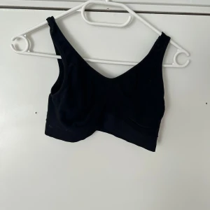 Svart croppad linnetopp, bh  - En enkel svart croppad linnetopp med breda axelband och djup urringning. Perfekt att styla till jeans eller kjol för en avslappnad look.