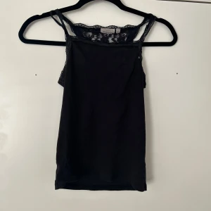 Svart ribbad linnetopp med spets båda för 20  - Svart ribbad linnetopp med smala axelband och spetsdetaljer upptill. Toppen har en feminin och enkel design som passar perfekt till sommaren.