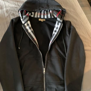 Burberry zip hoodie - Svart zip hoodie från burberry i storlek m men passar s den är i bra skick men ett litet syfel men inget man ser tydligt