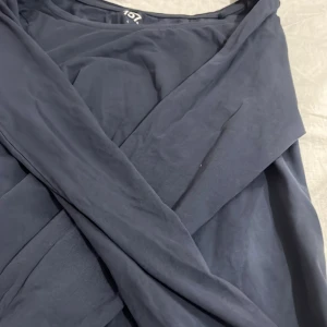 Mörkblå långärmad topp från 157 - Snygg mörkblå topp från 157 i storlek L. Toppen är tillverkad i mjuk bomull med lite stretch för extra komfort. Den har en omlottdesign som ger en schysst siluett och passar perfekt till dig som gillar stilrena plagg.