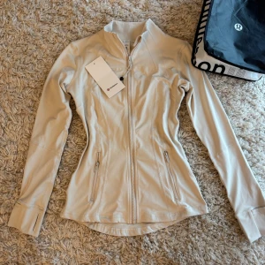 Define jacket Lululemon - Snygg beige träningsjacka från Lululemon med figurnära passform. träningsjacka är i storlek 4 som ungefär motsvarar S / M, beroende hur man vill att den ska sitta❤️ tröjan är helt ny och måste tyvärr sälja då storleken inte passar mig.