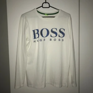 Hugo Boss tröja - Säljer vit boss tröja med blå svart text. Tröjan är i okej skick för att den är gammal. Tröjan är i tunn bomull. Storleken är S men kan passar XS lite bättre.