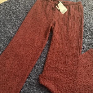 Vinröda mjukisbyxor från H&M XS - Säljer ett par helt nya vinröda byxor från H&M i storlek XS. Byxorna har en skön, strukturerad yta och resår i midjan med snörning. Perfekta för en chill look och riktigt bekväma att ha på sig.