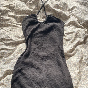 Svart kort klänning med halterneck - Säljer en svart kort klänning med snygg halterneck och ett diskret diamantformat mönster i tyget. Klänningen är ärmlös och har en smickrande passform som framhäver figuren. Perfekt för dig som gillar stilrena och trendiga plagg. Klänningen är storlek M, men passar mig som bär S.