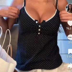 Blå prickig linnetopp med spets - Supersöt svart linnetopp med vita små prickar, smala axelband och dekorativa knappar framtill. Toppen har en v-ringad urringning med vit spetskant som ger en gullig touch. Perfekt till jeans eller kjol för en chill look.