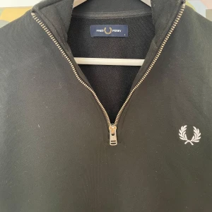 Fred Perry tröja - Svart långärmad tröja från Fred Perry med klassisk laurel-logga broderad på bröstet. Tröjan har en snygg half zip-dragkedja och står för en clean och stilren look. Kom privat för fler frågor och funderingar:)