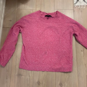 Rosa stickad tröja från Vero Moda - Mysig rosa stickad tröja från Vero Moda med rund halsringning och ribbade muddar. Perfekt för lager-på-lager och passar till både jeans och kjol. Långärmad och i en skön, mjuk kvalitet som håller dig varm under kyliga dagar.