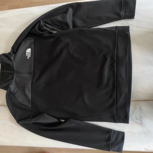 Svart fleece-tröja från The North Face - Svart långärmad fleece-tröja från The North Face med half zip och logga på bröstet.
