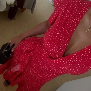 Röd omlottklänning med vita prickar - Superfin röd omlottklänning med vita prickar och volangkant nertill. Klänningen har korta ärmar, knyt i midjan och v-ringad hals. Perfekt för sommarens alla tillfällen och ger en riktigt söt och trendig look.