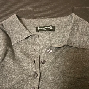 Grå stickad polotröja från Stradivarius - Mysig grå stickad polotröja från Stradivarius med klassisk krage och knappar framtill. Tröjan har lång ärm och är perfekt för lager-på-lager. Enkel och stilren design som funkar till många olika looks.