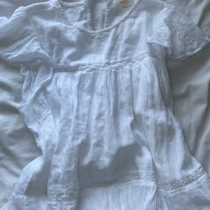 Vit blus från Gina Tricot - Säljer en söt vit blus från Gina Tricot i storlek 158/164. Blusen har korta ärmar, rund hals och fina spetsdetaljer vid midjan och nederkanten. Tillverkad i mjukt och luftigt linne, perfekt för varma dagar.