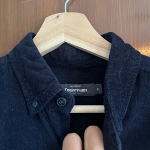 Mörkblå manchesterskjorta Dressmann S - Snygg mörkblå manchesterskjorta från Dressmann i storlek S. Skjortan har klassisk krage, knappstängning hela vägen och en bröstficka. Perfekt för dig som gillar en stilren och tidlös look med lite struktur i tyget.