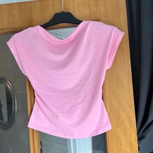Rosa topp med öppen rygg - Säljer en ljusrosa topp i mjuk bomull med korta ärmar och snygg öppen rygg. Toppen har en lösare passform och ett enkelt, stilrent snitt framtill. Perfekt för dig som vill ha en söt och trendig look med en twist.