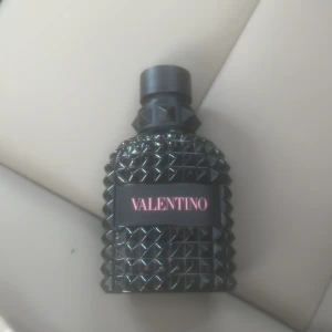 Valentino parfym svart nitar - Snygg parfymflaska från Valentino i svart glas med coolt nitat mönster och rosa logga på framsidan. Flaskan har en robust, lyxig känsla och sticker ut med sin unika design. Perfekt för dig som gillar statement-detaljer på sminkbordet.