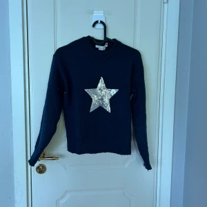 Mörkblå stickad tröja med stjärna - Mysig mörkblå stickad tröja från Gina Tricot med lång ärm och en stor glittrig silverstjärna framtill. Perfekt för dig som gillar att sticka ut lite extra. Rund halsringning och ribbade muddar ger en skön passform.