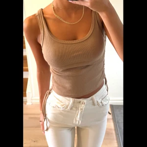 Beige ribbad linnetopp med snörning - Snygg beige ribbad linnetopp med rund halsringning och smala axelband. Toppen har snörning i sidorna som ger en trendig look och gör det enkelt att justera passformen. Perfekt till jeans eller kjol för en chill stil.