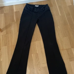 Svarta bootcut byxor Gina Tricot 158 - Svarta bootcut byxor från Gina Tricot i storlek 158. Byxorna har hög midja, pressveck framtill och två knappar i midjan. Snygg passform med utsvängda ben och bälteshällor. Perfekta för en clean och stilren look.