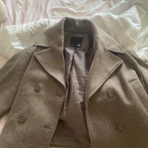 Beige croppad rock från 157, XS - Säljer en beige croppad rock från 157 med breda slag, dubbelknäppning och snyggt foder. Jackan har en klassisk look men är kortare i modellen vilket ger en modern vibe. Perfekt att slänga över en outfit för extra stilpoäng.