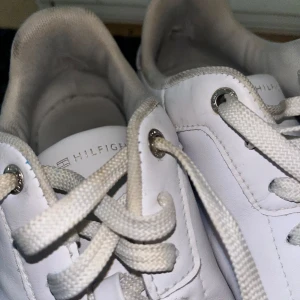 Vita sneakers från Tommy Hilfiger - Snygga vita sneakers från Tommy Hilfiger med klassisk design. Skorna har snörning, rund tå och är tillverkade i skinn. Detaljer som metallögla och logga på tungan samt sula med stjärnmönster. Perfekta för en clean och stilren look.