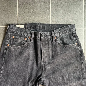 Levi's 501 jeans - Svarta Levi's 501 jeans i klassisk straight fit med fem fickor och knappgylf. Jeansen är tillverkade i robust denim och har en mörk tvätt som ger en cool vintagekänsla. Perfekta för dig som gillar tidlös stil och vill ha ett par jeans som funkar till allt.